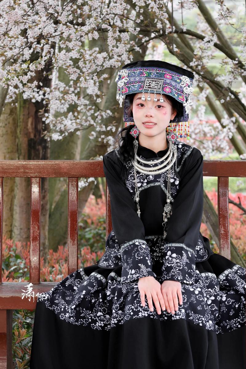 布依族服飾美美美.她身著精致的民族服飾端坐于此,黑色衣料上的